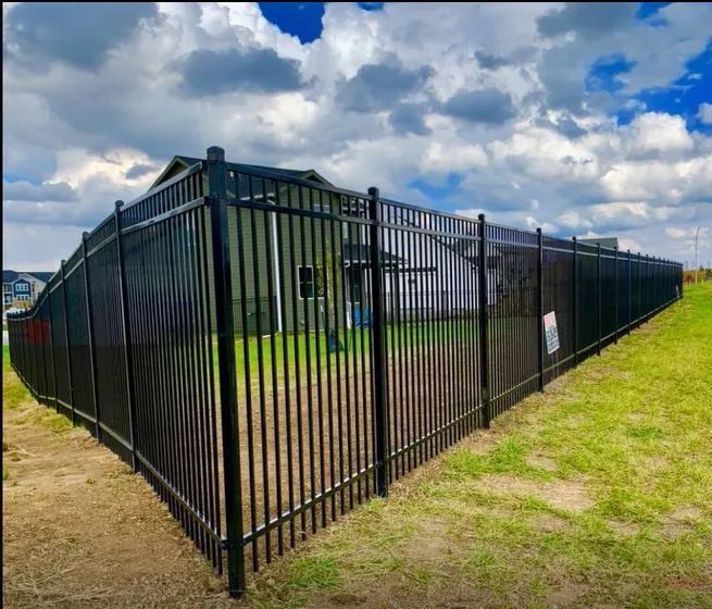 A black metal fence surrounds a grassy field in front of a house.