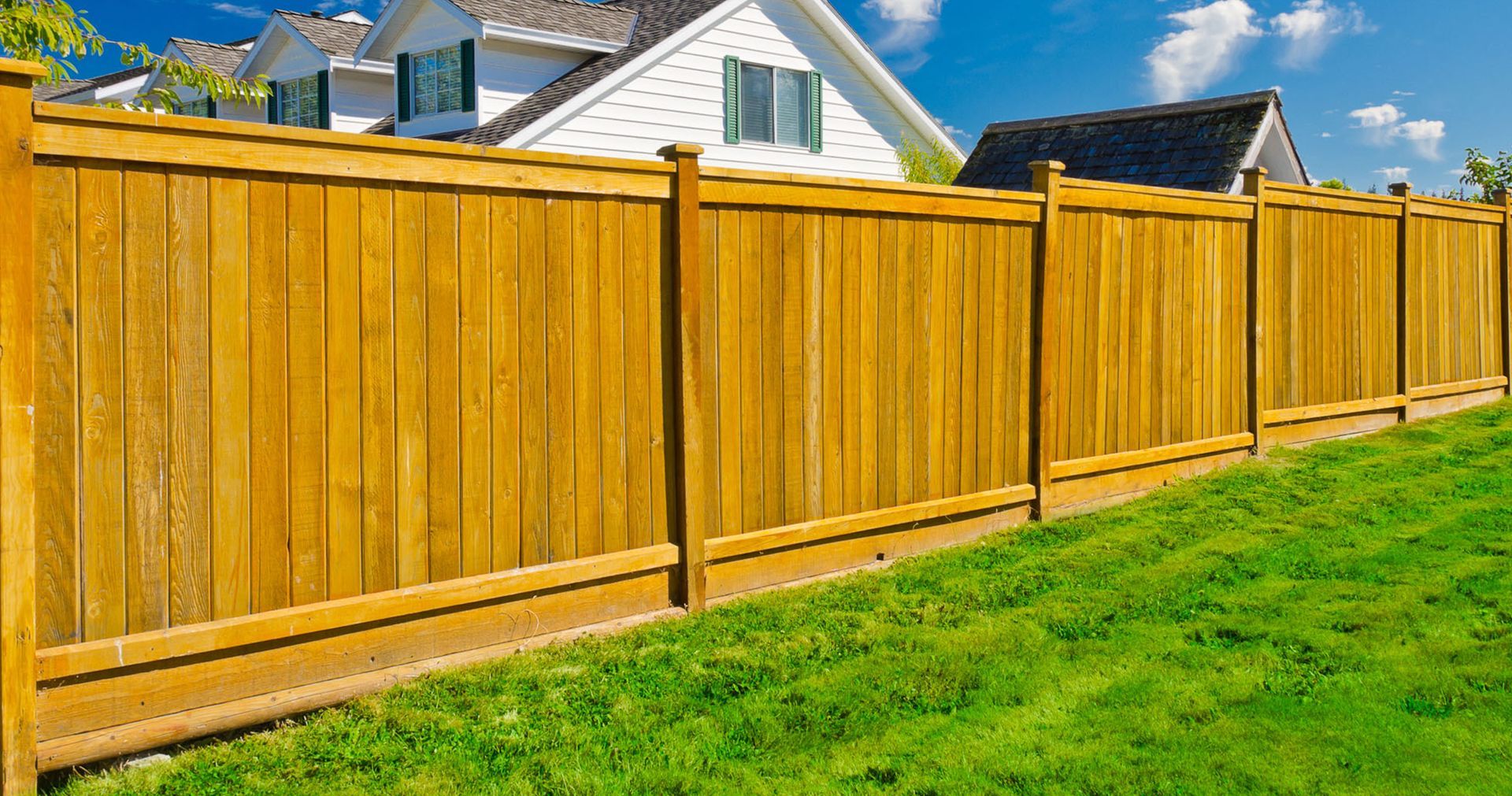 A wooden fence surrounds a lush green lawn in front of a house.