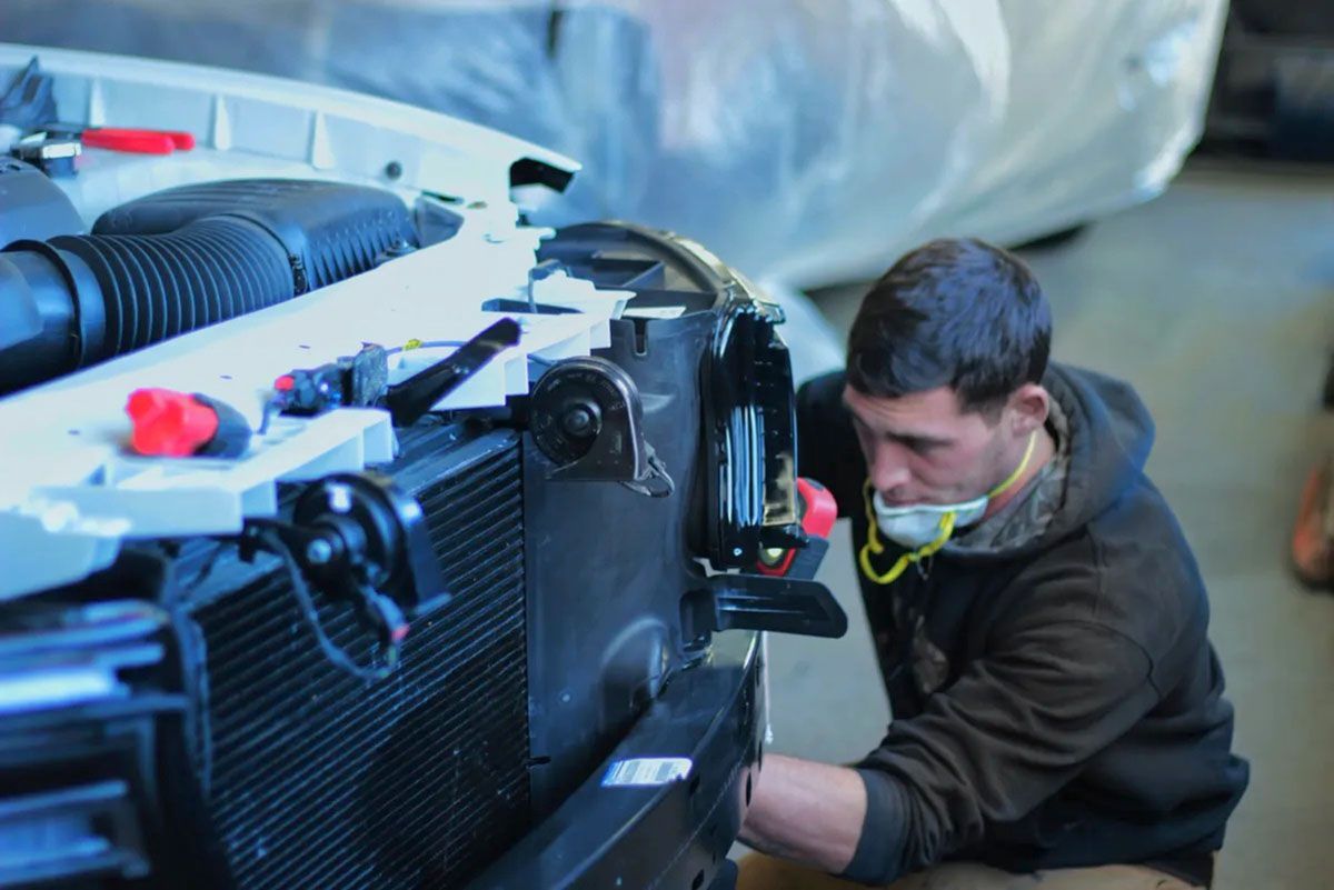 A man wearing a mask is working on the front of a car