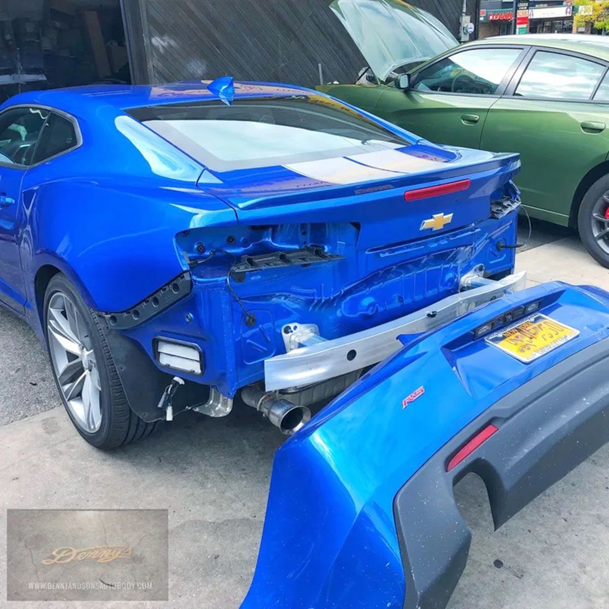 A blue car with a damaged bumper is parked next to a green car