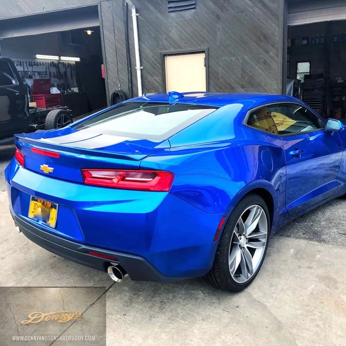 A blue chevrolet camaro is parked in front of a garage
