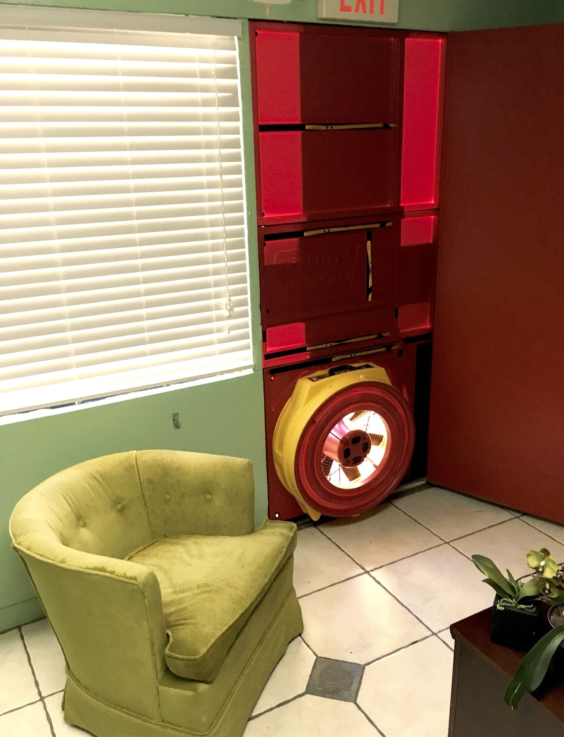 A room with a green chair and a red exit sign