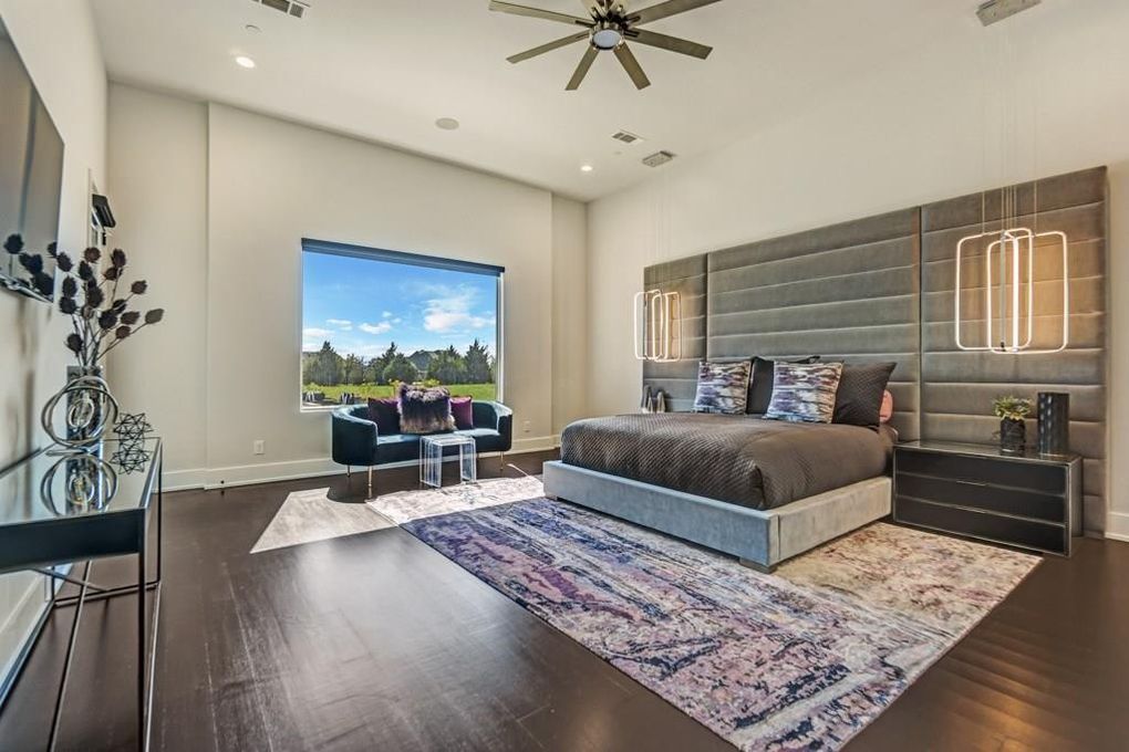 A bedroom with a king size bed, a rug, a ceiling fan and a large window.