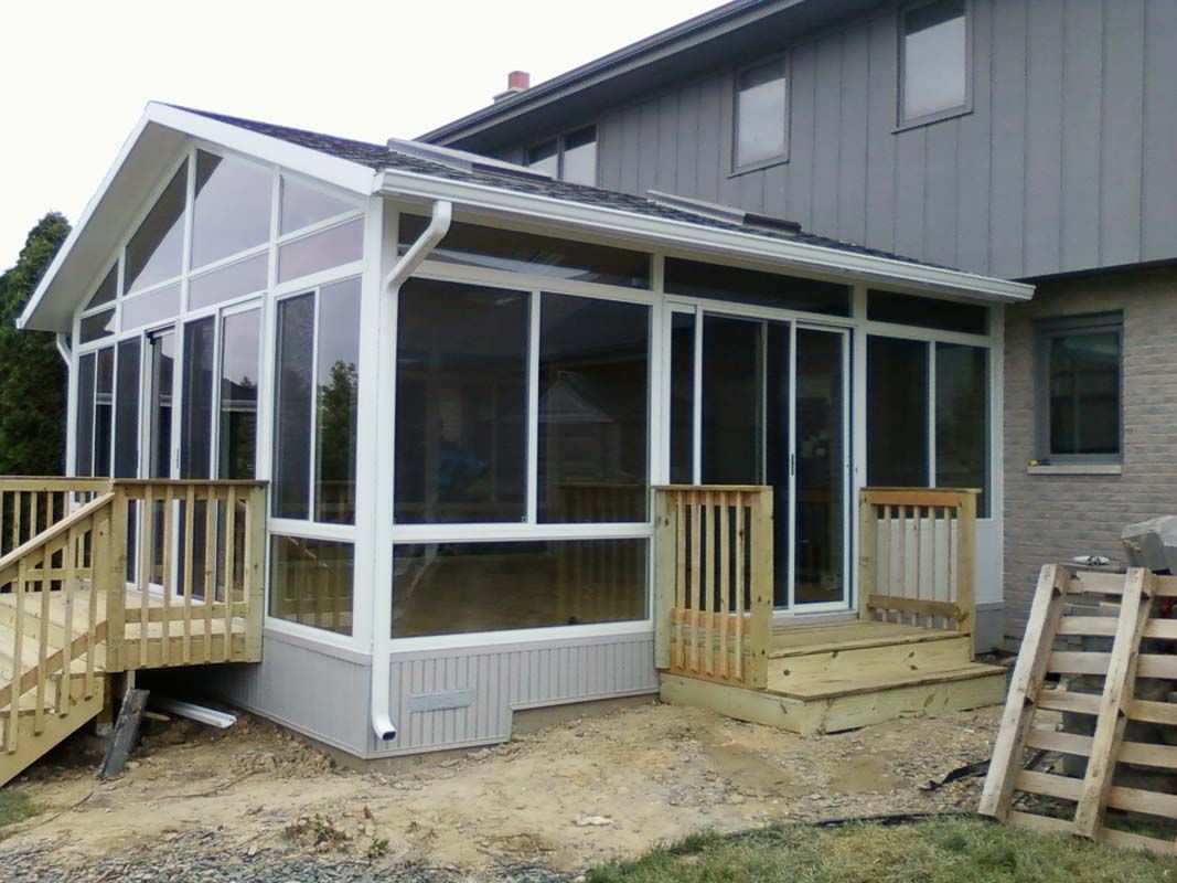 A screened in porch with a wooden deck next to a house