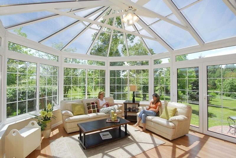 Two women are sitting on couches in a living room with lots of windows.