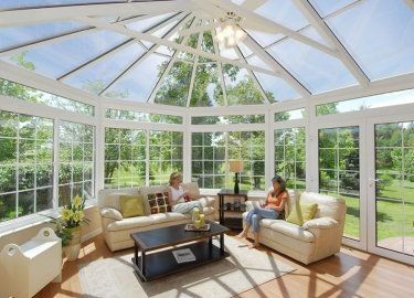 Two people are sitting in a living room with a lot of windows.