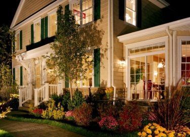 A large house with green shutters is lit up at night.