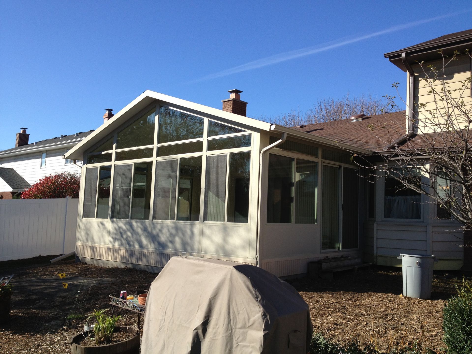 A house with a sunroom and a grill in the backyard.