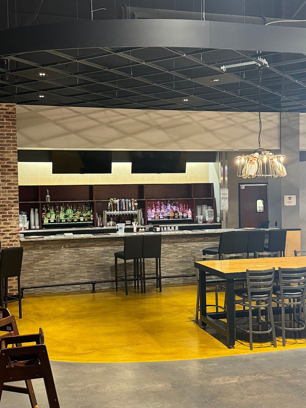 A restaurant with a yellow floor , tables , chairs and a bar.