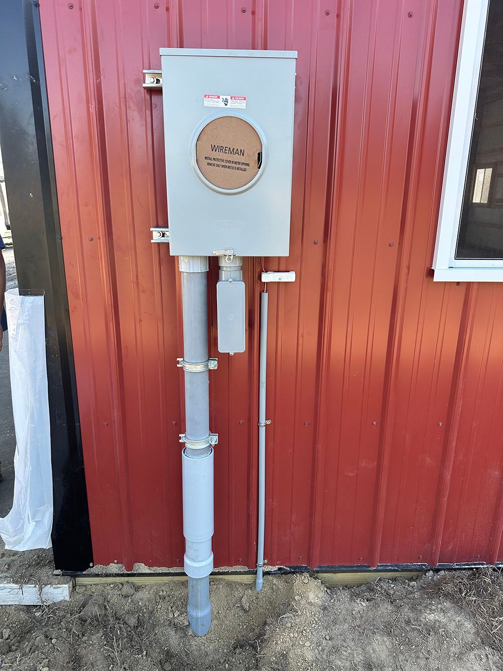 An electrical box is sitting on the side of a red building.
