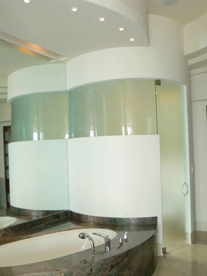 Curved white walls with glass panels separate a bathroom, with a bathtub in the foreground.