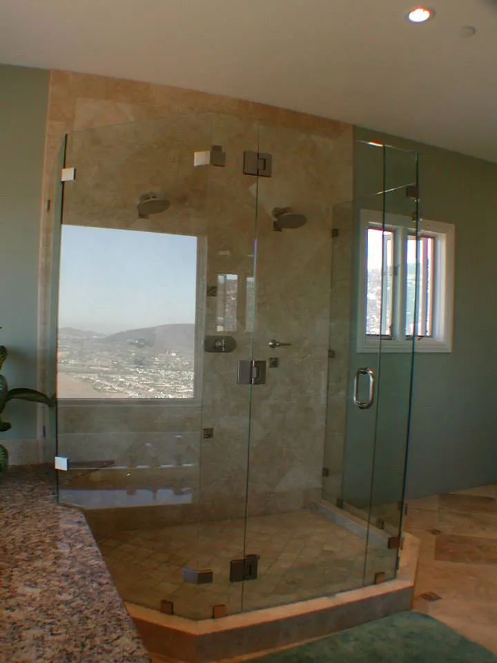 Glass shower enclosure with a window overlooking a cityscape. Beige tile walls and green accents.