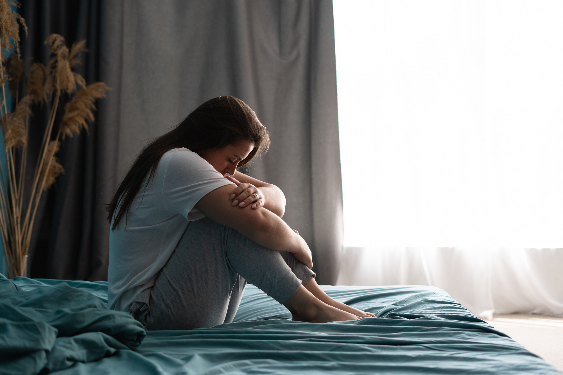 a person sitting on a bed in front of a window experiencing grief