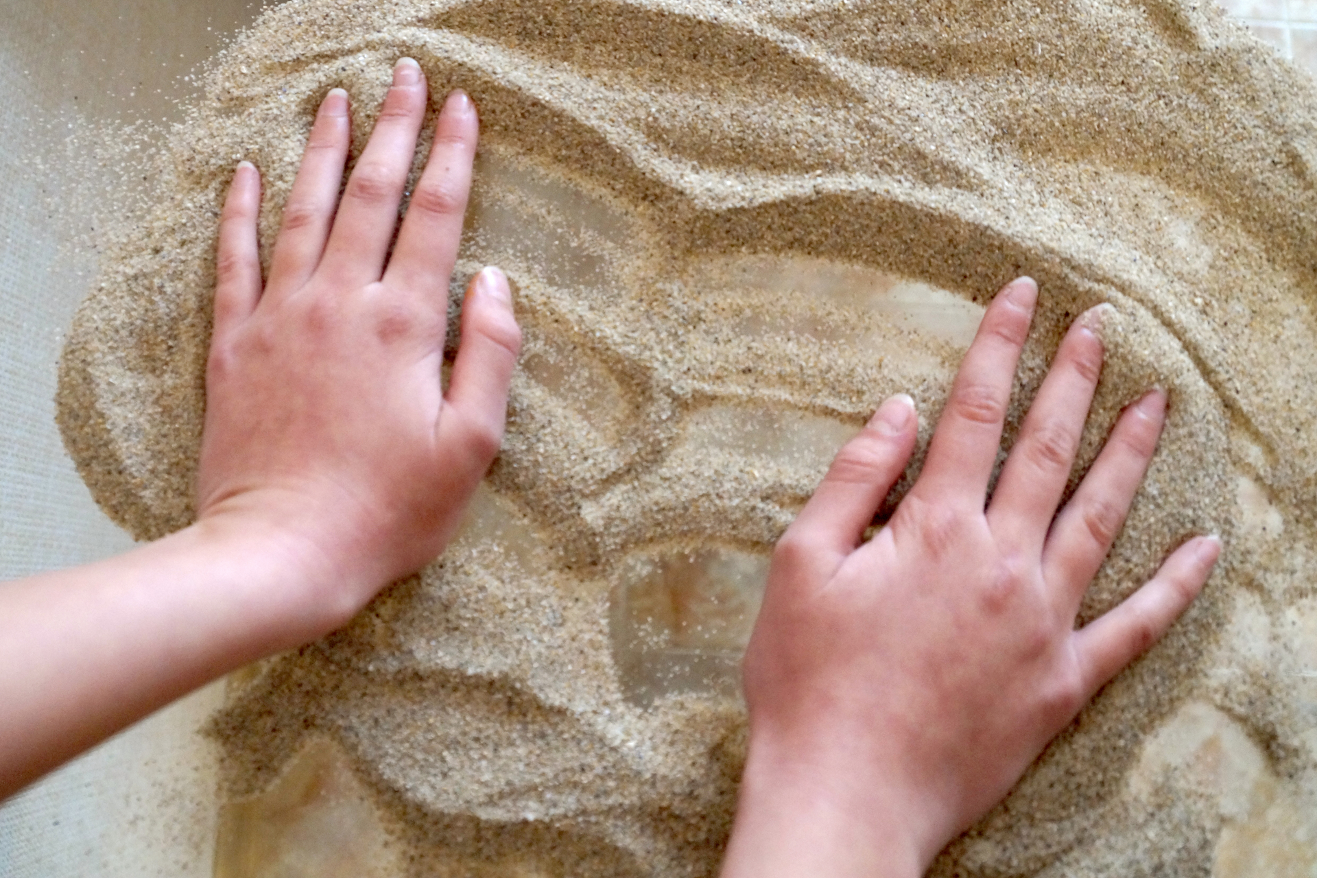 Close-up of hands arranging sand in a  tray, part of a therapeutic Sand Tray Therapy session.