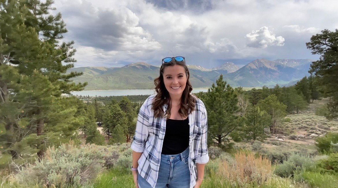 Lisa, Coastal Wellness intern, smiling amidst scenic mountains, portraying mental health positivity.