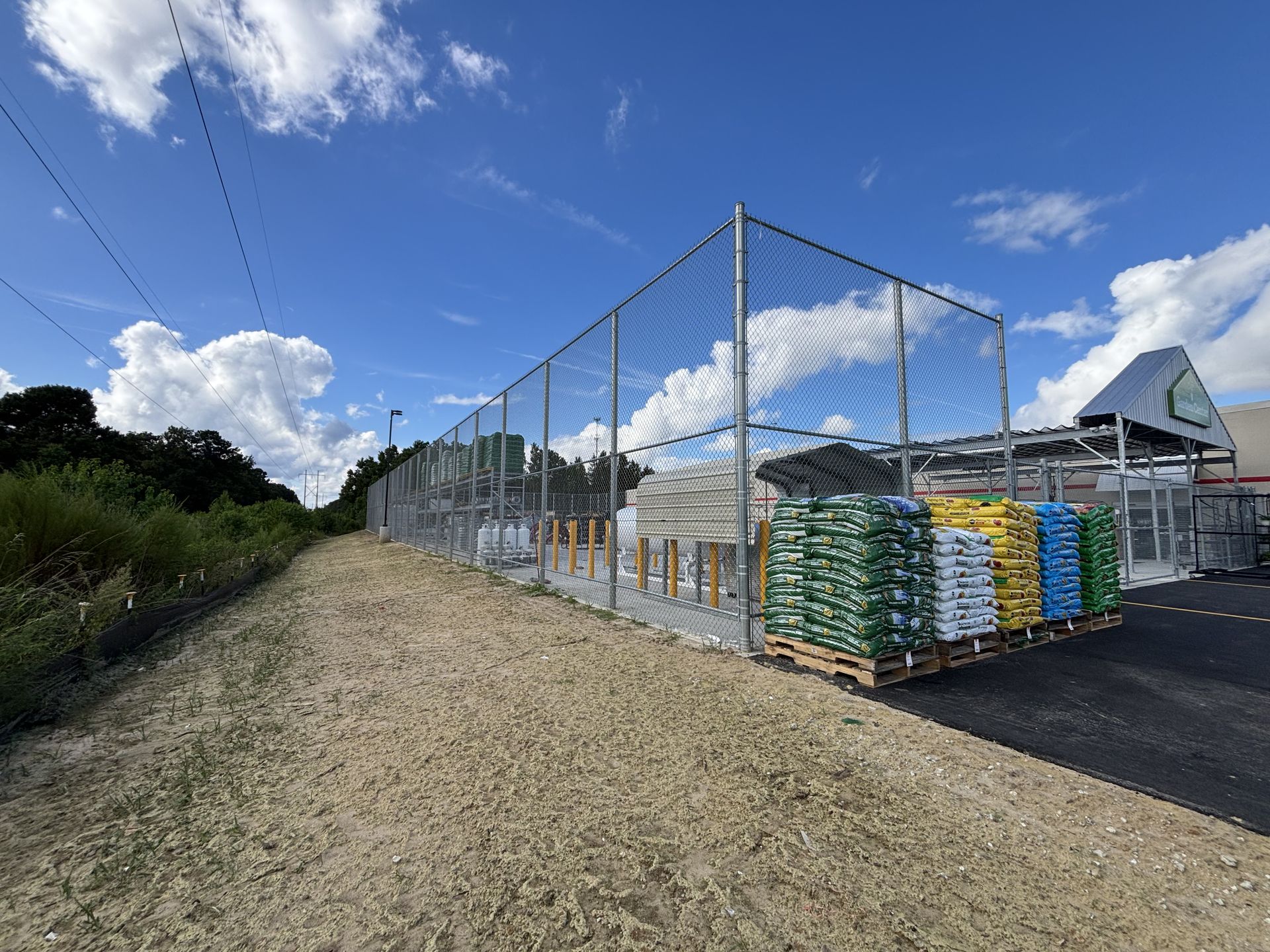 Metal fence encloses bags of materials outside a store under a partly cloudy sky.