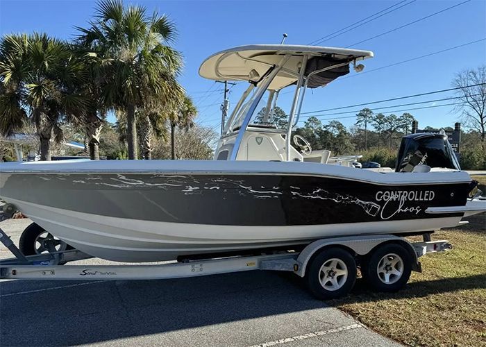 Black and white boat on a trailer, parked outdoors under a blue sky with palm trees.