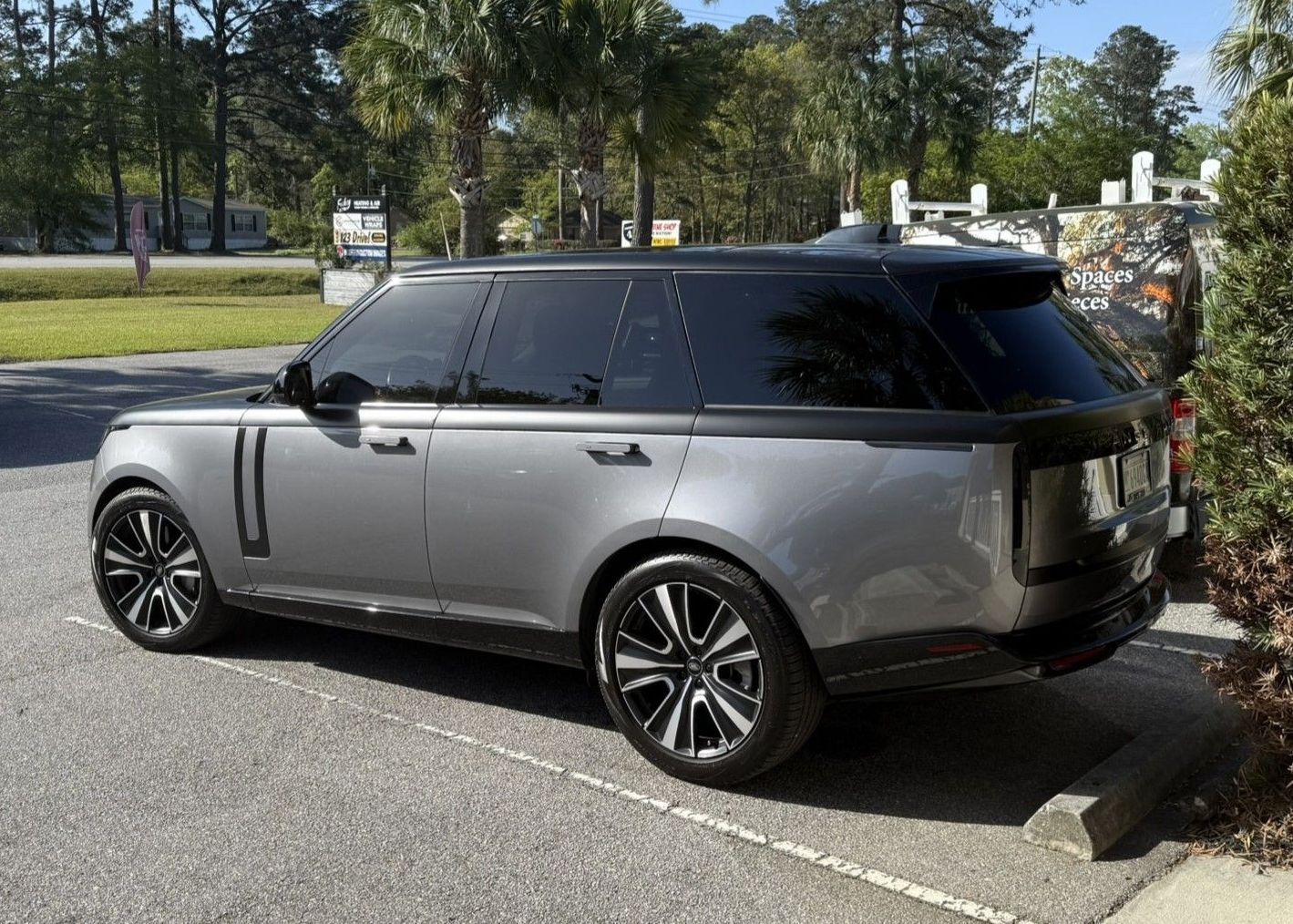 Two-tone gray SUV parked in a lot beside a sidewalk and trees