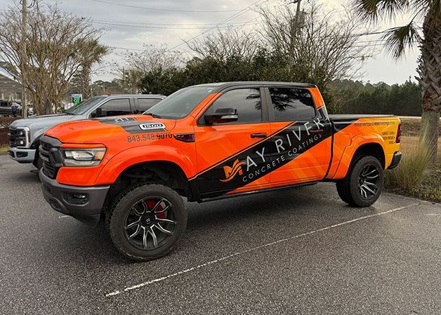 Orange lifted pickup truck with black racing graphics parked in a lot