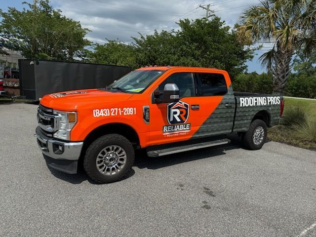 Orange-and-black roofing company pickup truck parked on a street, with “ROOFING PROS” on the side.