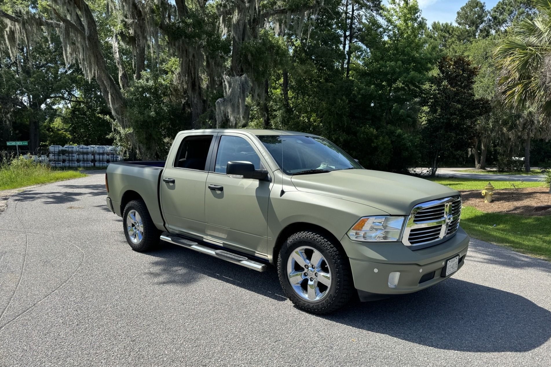 Olive green Ram pickup truck parked on gravel driveway, with trees in the background.