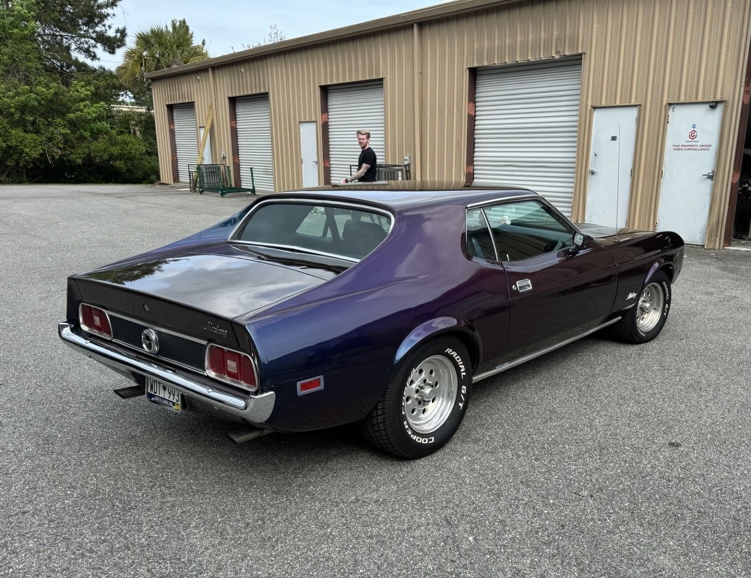 Dark blue 1971 Ford Mustang Mach 1 in front of a tan garage.