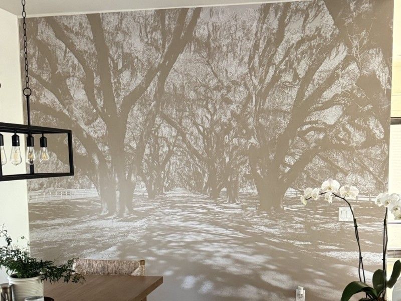 Large wall mural of sunlit trees; dining area with light fixture, orchids, and table.