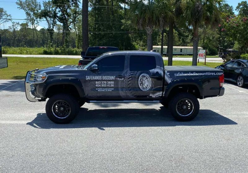 A lifted black Toyota Tacoma truck with business logos on the side, parked outside.