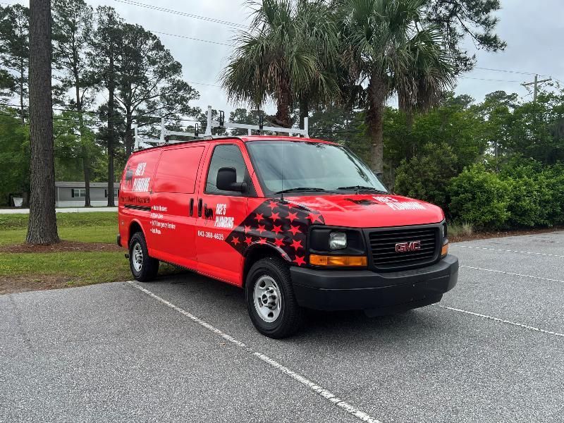 Red GMC service van parked in a lot. Black stars on the side, roof rack, trees in background.