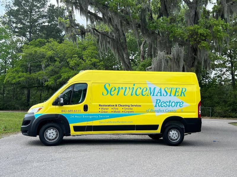 Yellow ServiceMaster van parked on a road with green trees in the background.