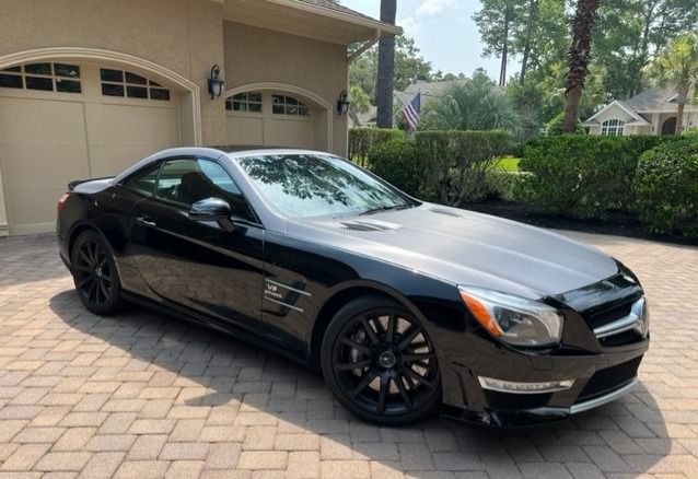 Black Mercedes-Benz SL AMG sports car parked on a brick driveway in front of a garage.