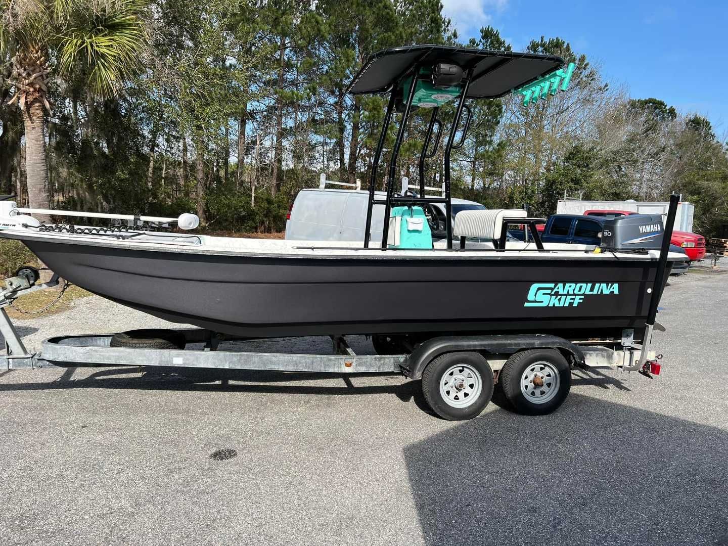 Carolina Skiff boat on trailer, black hull, turquoise logo, canopy, parked outdoors.