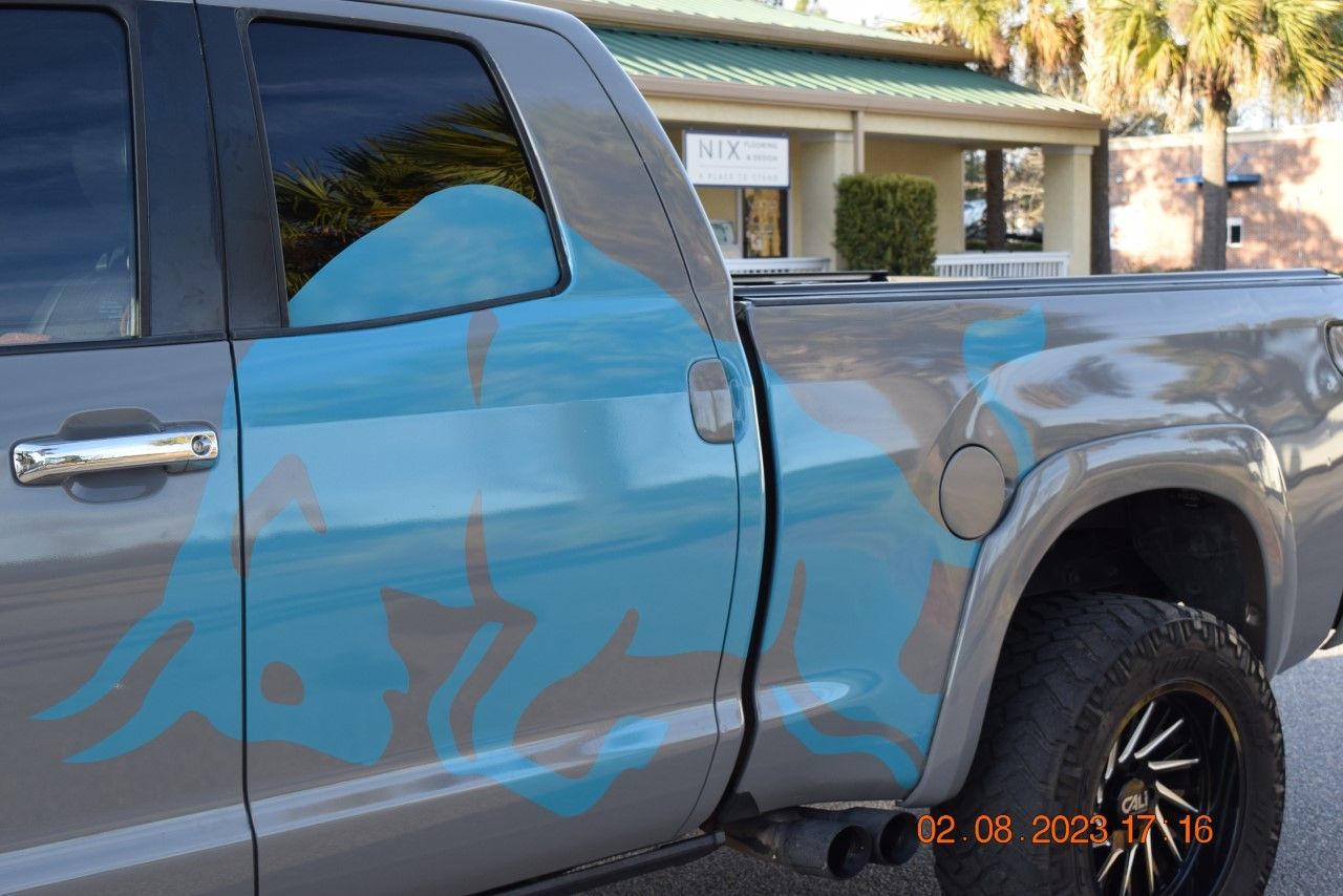 Gray pickup truck with blue and gray flame design. Black wheels and exhaust pipes.