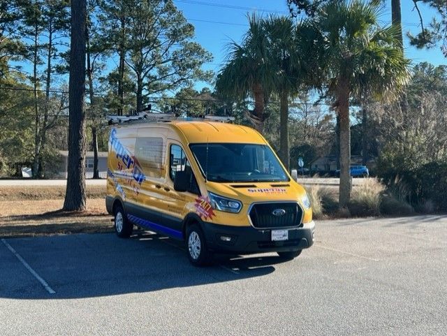 Yellow service van parked outdoors. Trees in background.