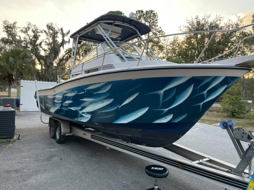 Boat on a trailer, featuring a painted mural of swimming fish on the hull; outdoors.