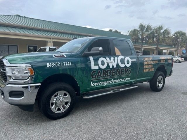 Green LowCo Gardeners truck parked in front of a building with a green roof.