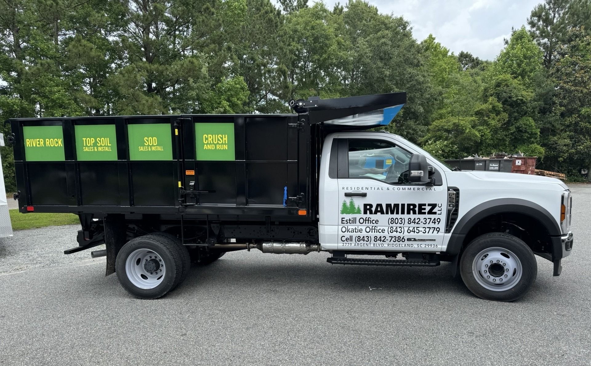 White and black dump truck with green logos for Ramirez Landscaping, parked on asphalt.