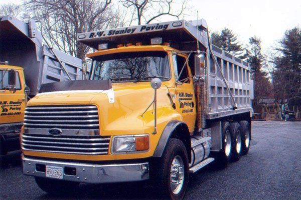 A yellow dump truck from stanley paving is parked in a parking lot