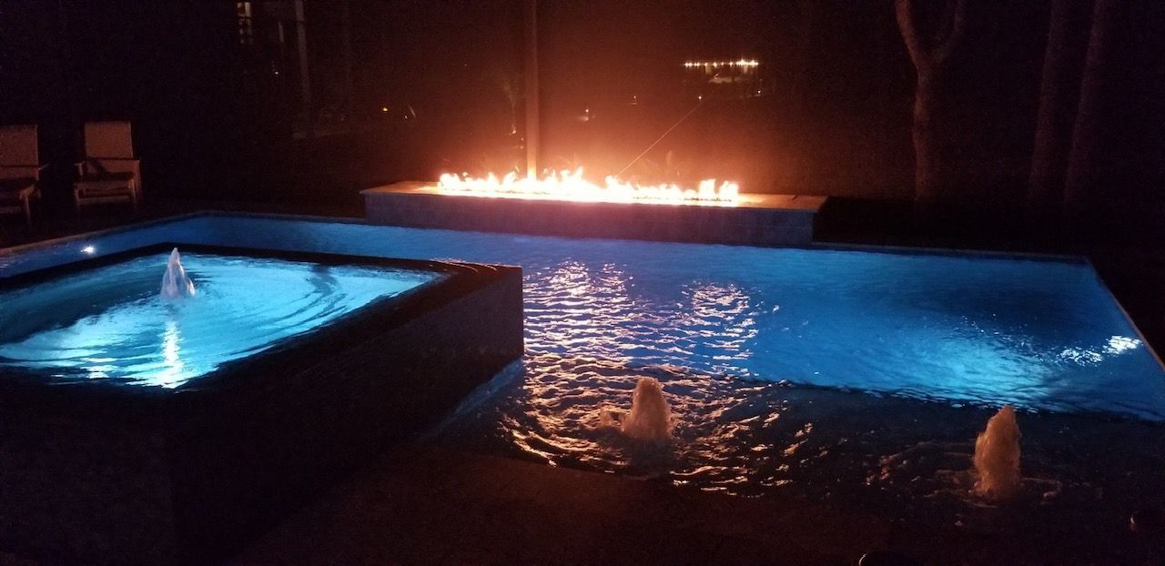 A swimming pool with a fire pit in the middle of it at night
