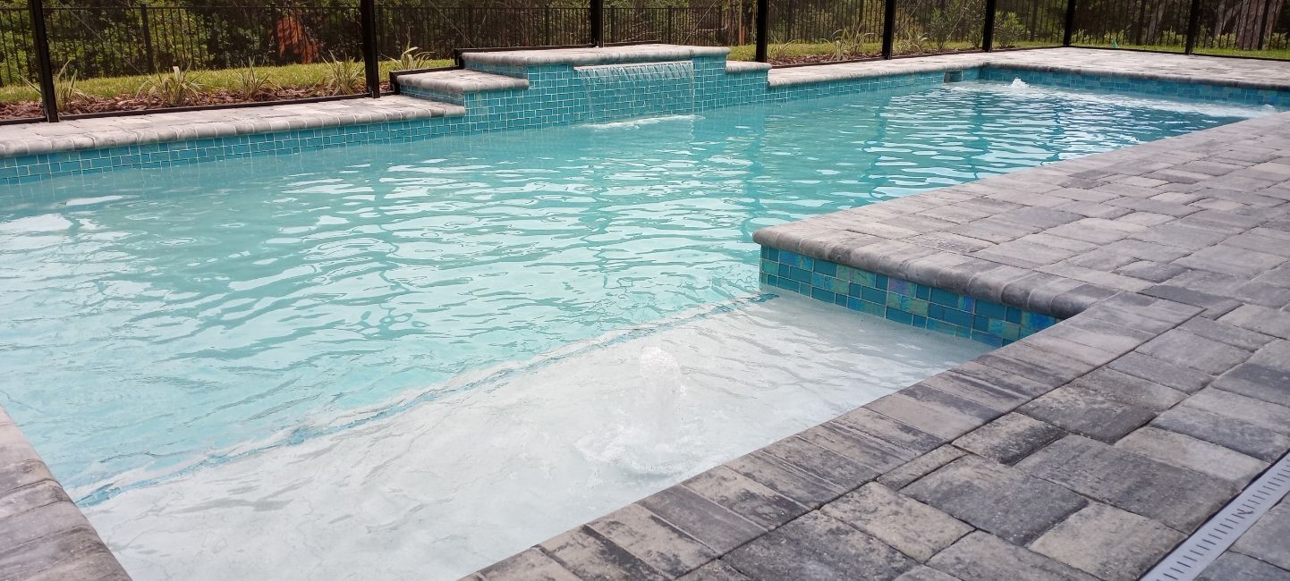 A large swimming pool surrounded by a brick patio and a fence