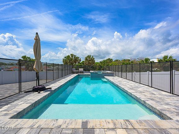 A large swimming pool surrounded by a fence and umbrella on a sunny day