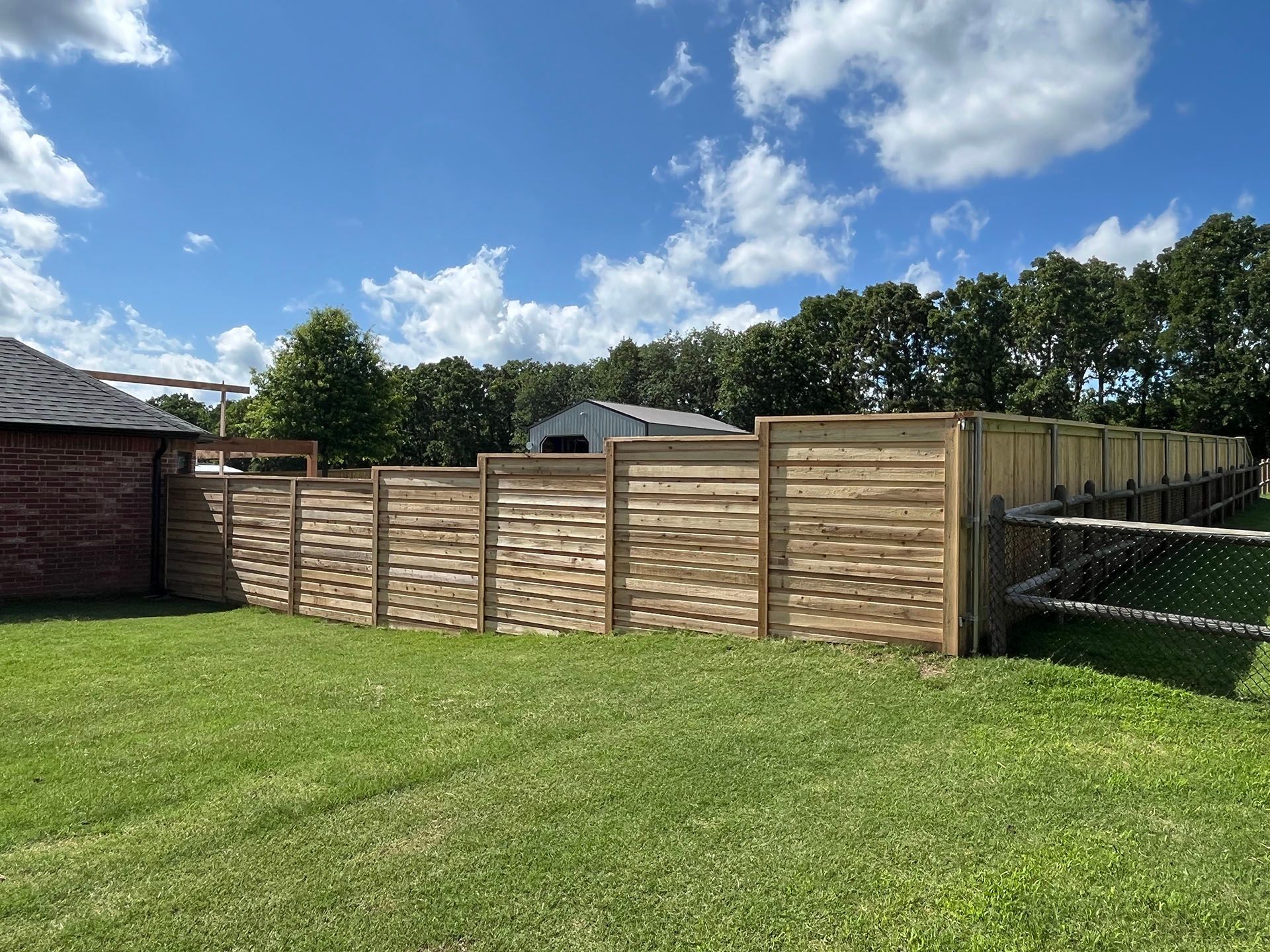 A wooden fence is in the middle of a lush green field.