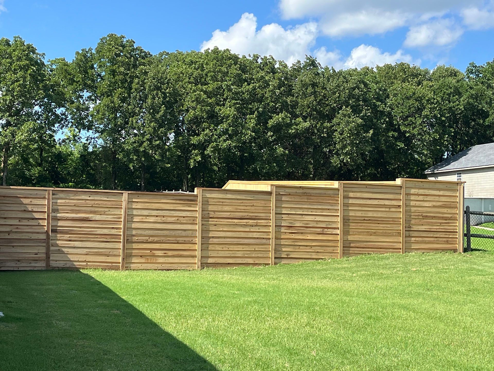 A wooden fence is in the middle of a lush green field.