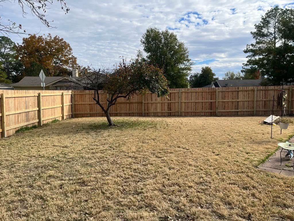 A backyard with a wooden fence and a tree in the middle.