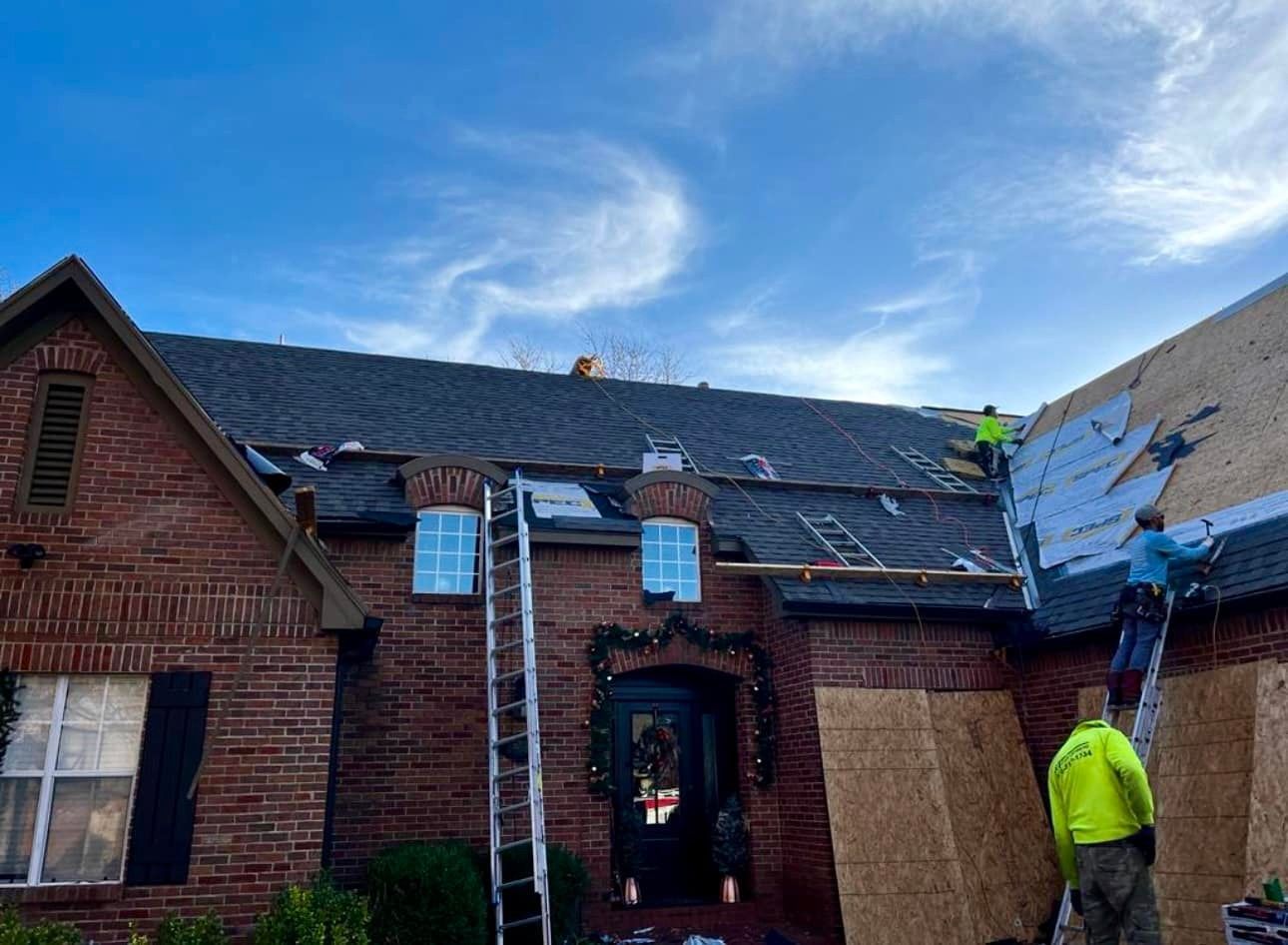 A group of men are working on the roof of a brick house.