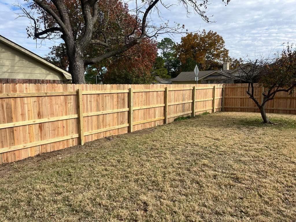 A wooden fence is in the backyard of a house.