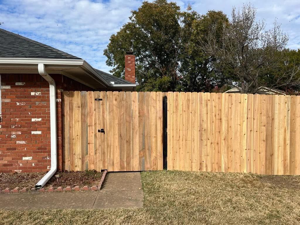 A wooden fence with a gate in front of a brick house.