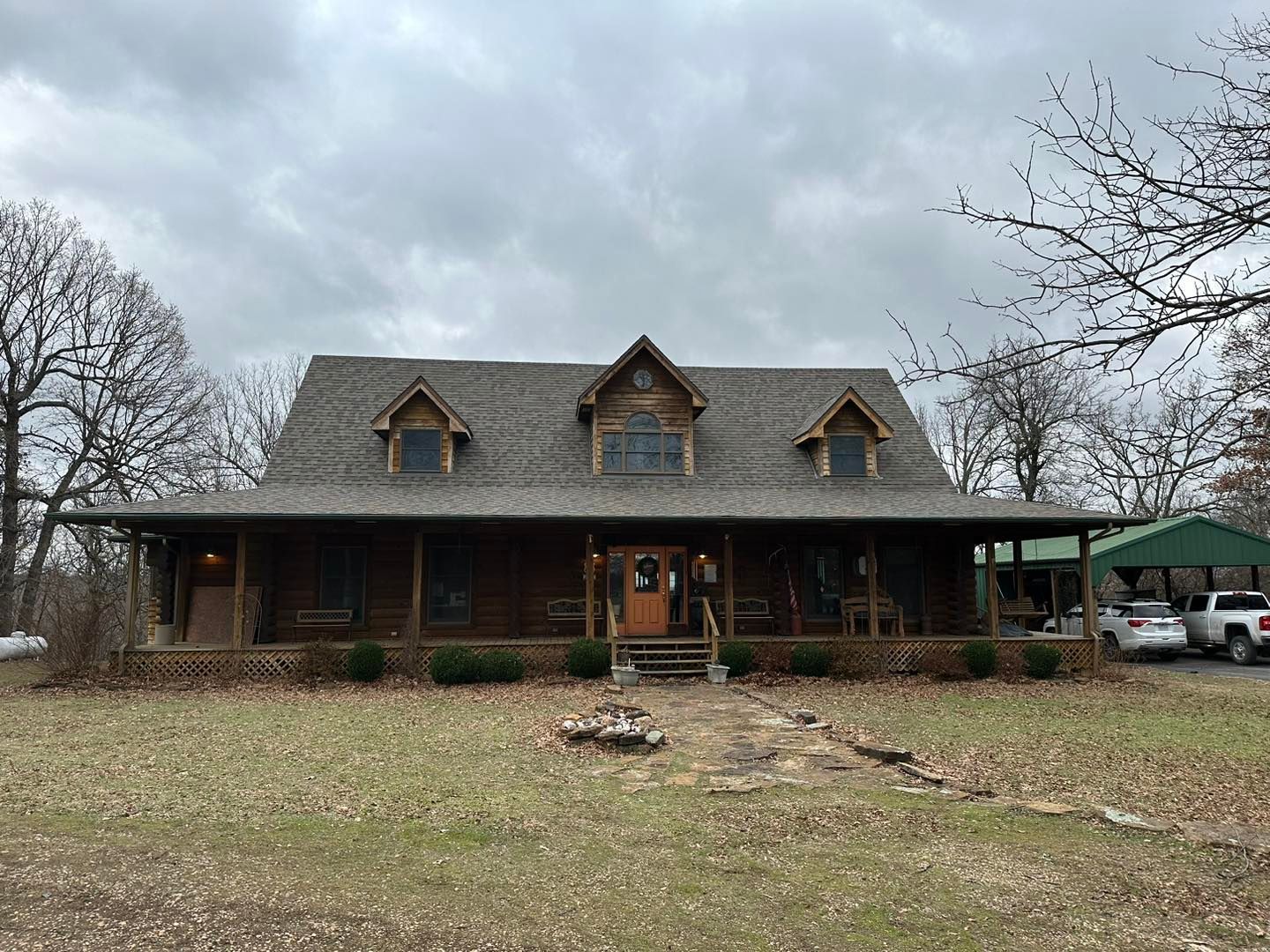 A large house with a porch and a carport in the middle of a field.