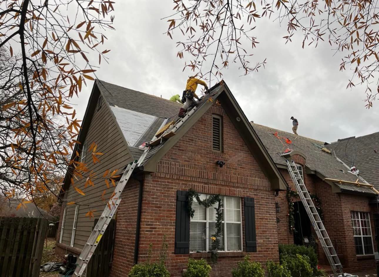A group of people are working on the roof of a brick house.