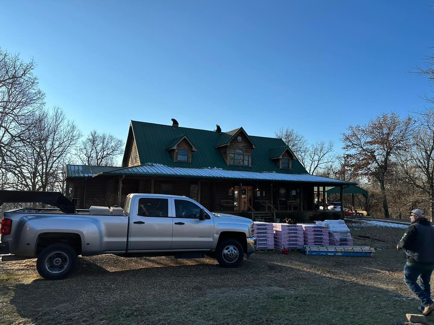 A silver truck is parked in front of a house with a green roof.